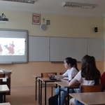 uczniowie siedzą w ławkach w sali lekcyjnej, oglądają prezentację