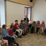 Dzieci siedzą w kręgu i słuchają informacji o Muzeum Wojska