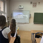 Uczniowie stoją tyłem, śpiewają, na tablicy interaktywnej wyświetlone słowa ''Roty''.jpg
