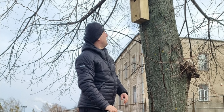 mężczyzna wiesza  budkę dla ptaków  na drzewie.jpg