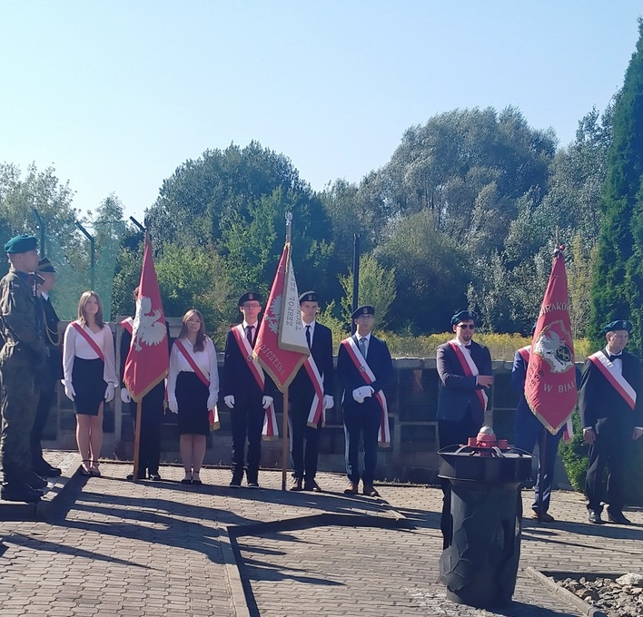 dziewczynki i chłopak stoją ze sztandarem w miejscu składania kwiatów.jpg