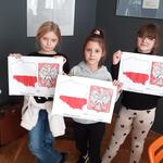 Trzy dziewczynki pokazują pokolorowane godło Polski oraz wyklejony kontur Polski w postaci flagi. .jpg