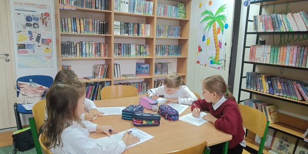 uczniowie siedzą przy stoliku w bibliotece